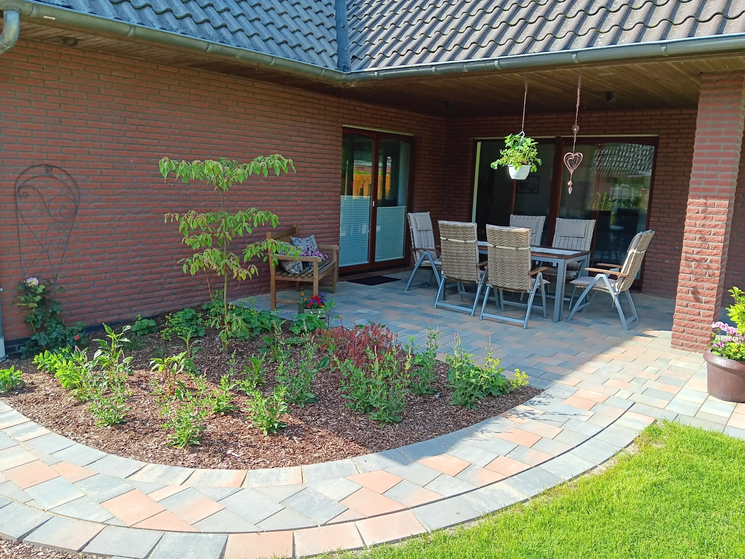 Ein Sitzbereich im Freien mit einem Tisch und Stühlen, umgeben von Gartenpflanzen und einem gepflasterten Boden.